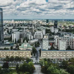 Widok z lotu ptaka na warszawskie osiedle z blokami mieszkalnymi i wieżowcami w tle.