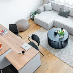 Nowoczesny salon z szarą kanapą, drewnianym stołem i czarnymi krzesłami.