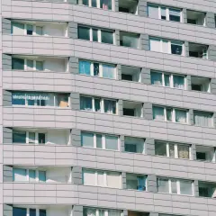 Szara fasada bloku mieszkalnego z wieloma oknami i balkonami.