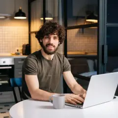 Mężczyzna z kręconymi włosami pracuje na laptopie w kuchni.