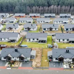 Widok z lotu ptaka na osiedle nowoczesnych domów jednorodzinnych z szarymi dachami, otoczonych lasem.