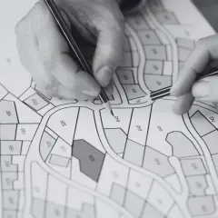 Dłonie z ołówkami nad mapą działek z numerami.