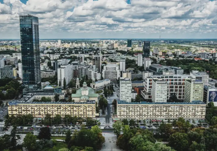 Widok z lotu ptaka na warszawskie osiedle z blokami mieszkalnymi i wieżowcami w tle.