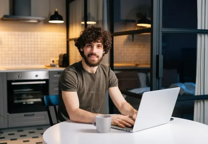 Mężczyzna z kręconymi włosami pracuje na laptopie w kuchni.