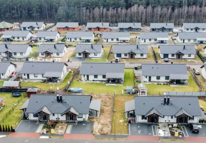 Widok z lotu ptaka na osiedle nowoczesnych domów jednorodzinnych z szarymi dachami, otoczonych lasem.