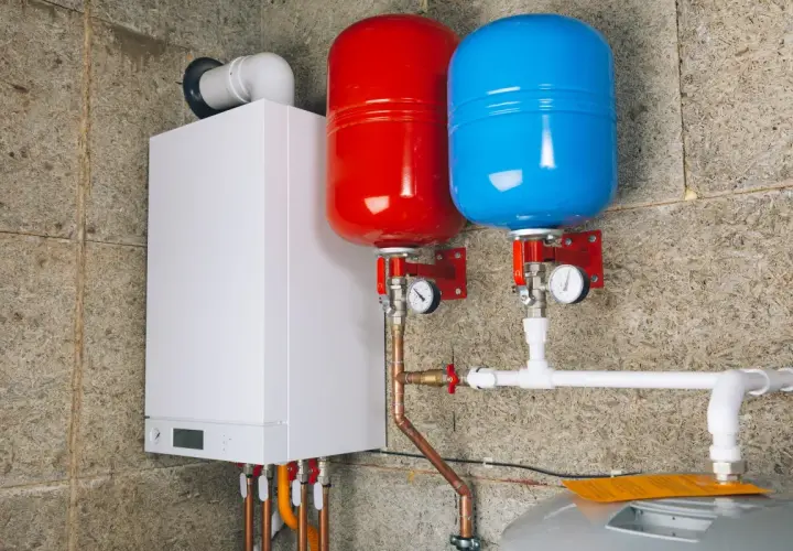 Biały piecyk gazowy z dwoma zbiornikami (czerwonym i niebieskim) oraz instalacją hydrauliczną.