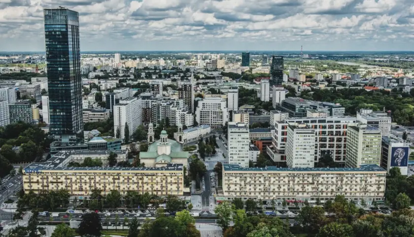 Widok z lotu ptaka na warszawskie osiedle z blokami mieszkalnymi i wieżowcami w tle.