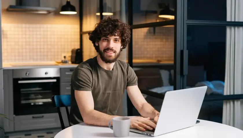 Mężczyzna z kręconymi włosami pracuje na laptopie w kuchni.