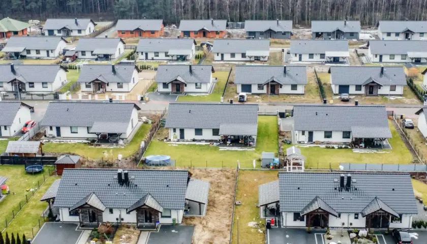 Widok z lotu ptaka na osiedle nowoczesnych domów jednorodzinnych z szarymi dachami, otoczonych lasem.
