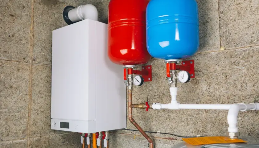 Biały piecyk gazowy z dwoma zbiornikami (czerwonym i niebieskim) oraz instalacją hydrauliczną.