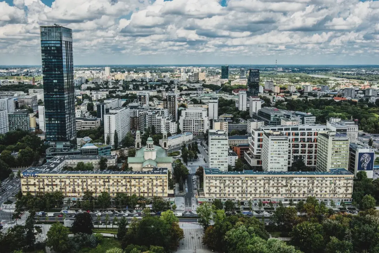 Widok z lotu ptaka na warszawskie osiedle z blokami mieszkalnymi i wieżowcami w tle.