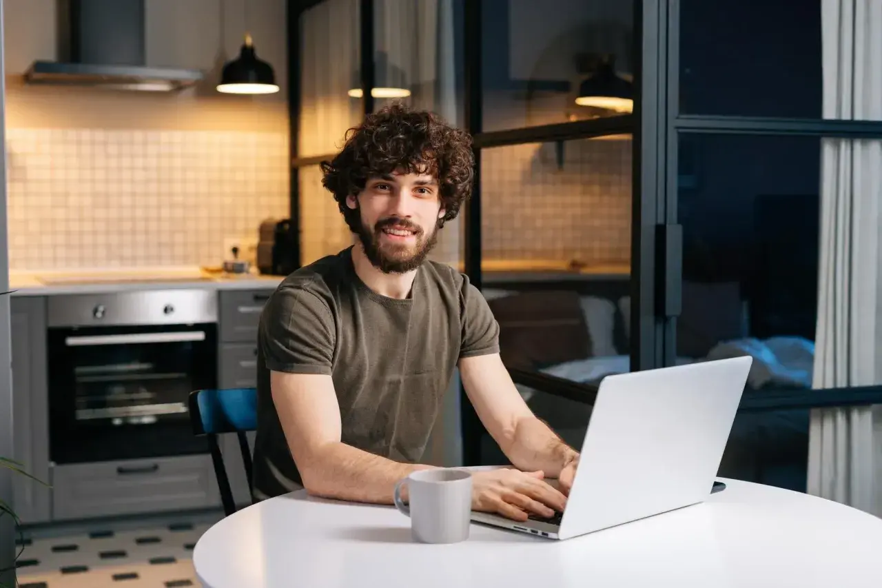 Mężczyzna z kręconymi włosami pracuje na laptopie w kuchni.